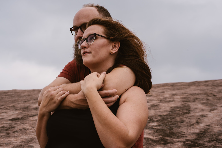 Man wrapping his arms around his fiance from behind at their engagement session at Enchanted Rock.